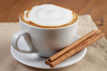 cup of fresh hot cappuccino with cinnamon sticks