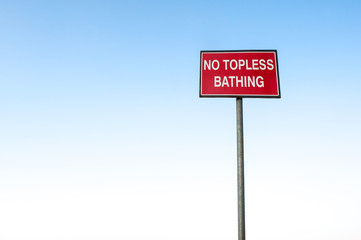 No topless bathing sign post against clear blue sky