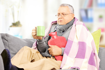 Ill man on a sofa covered with blanket drinking hot tea at home