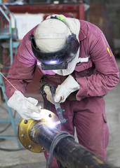 Man in a safety suit is welding a metal pipe