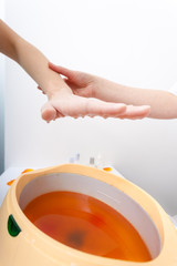 Female hand and orange paraffin wax bowl. Woman in beauty salon