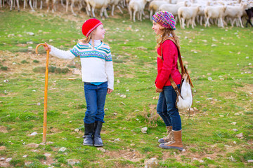 Kid girl shepherdess sisters happy with flock of sheep and stick