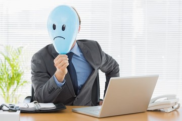 Businessman holding sad smiley faced balloon at office
