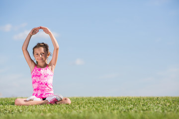 A girl sitting on the green grass in lotus pose
