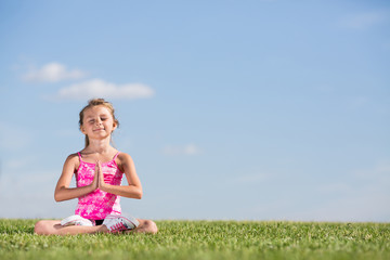 A girl sitting on grass in lotus pose with eyes closed