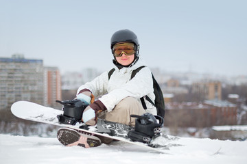 Fototapeta na wymiar Smiling girl snowboarder in helmet sitting with snowboard
