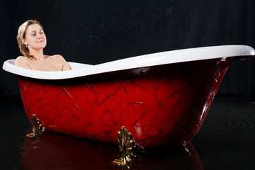 Beautiful smiling girl relaxes in the red bathtub