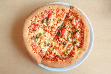 Pizza is cut into pieces with tomatoes, cheese and herbs