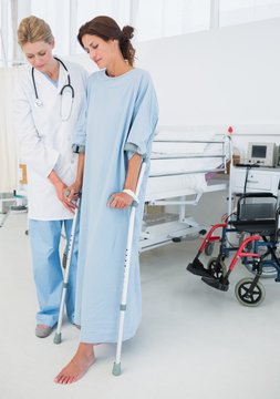 Doctor Helping Patient In Crutches At Hospital