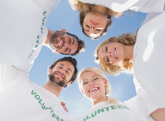 Fototapeta na wymiar Happy volunteers forming a huddle against blue sky