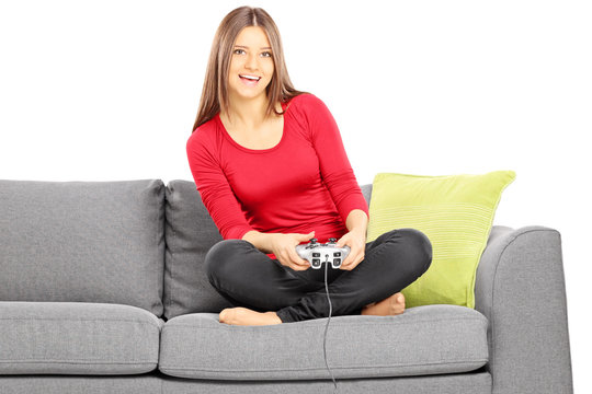 Young smiling female sitting on a couch and playing video game