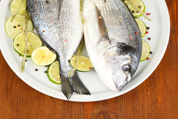 Two fish dorado with lemon on plate on wooden table close-up