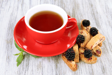 Cup of tea with cookies and blackberry on table close-up