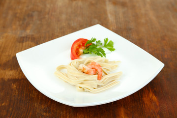 Pasta with shrimps on white plate, on wooden background