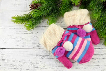 Striped mittens with fir branches on wooden background