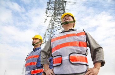 two workers standing before electrical power tower