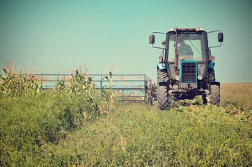 Fototapeta premium Old tractor mowing corn in the field close-up toning vintage eff