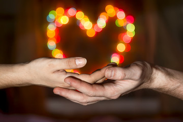 Women's hands in the men's hands holding a heart shaped bokeh