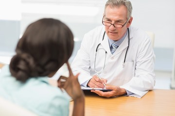 Mature doctor listening to his patient and taking notes