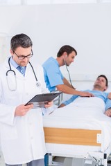 Doctor writing reports with patient and surgeon in background