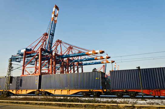 Güterzug mit Containern auf Schienen vor Hafenkränen im Industriegebiet