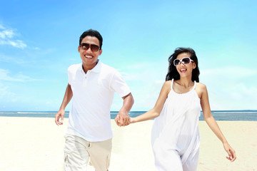 Beach couple in white dress running having fun laughing together