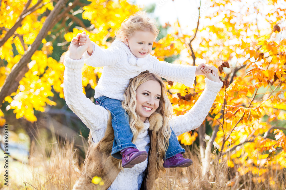 Wall mural Young mother playing with her daughter in autumn park