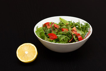 Light salad with tomatoes in white china bowl and lemon