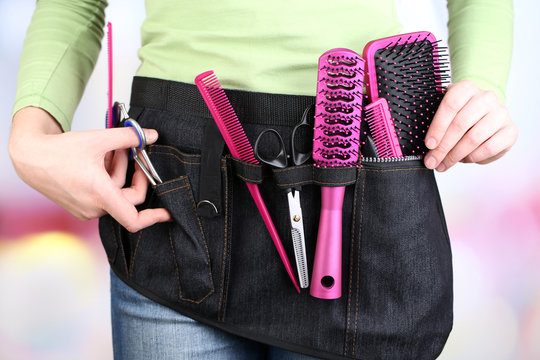 Woman hairdresser with tool belt on bright background