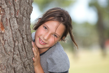 girl looking from behind a tree