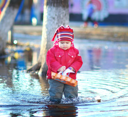 Little cheerful girl 2-3 years, runs the boats in the spring pud