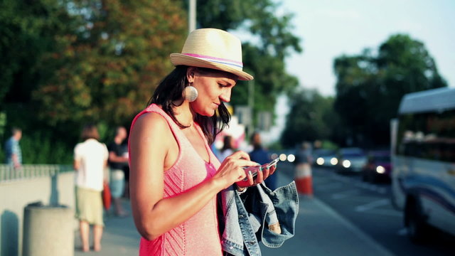 woman standing at the bus stop and using a cellphone