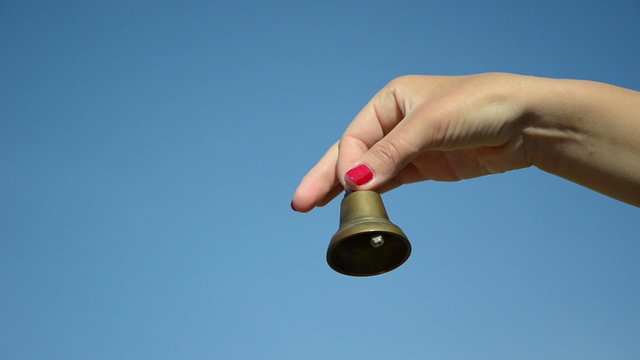 Girl hand with red nails shake small iron bell on blue sky