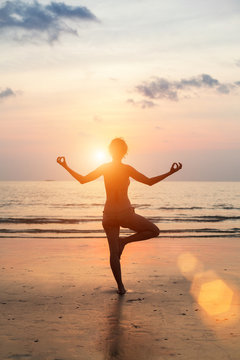 Silhouette of a beautiful yoga woman on the beach at sunset.