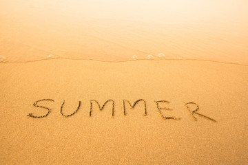 Summer - text written by hand in sand on a beach