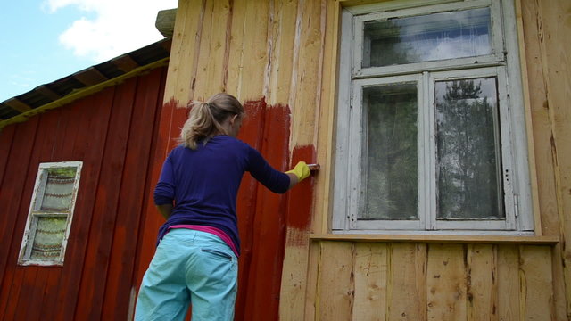 Painter girl paint rural house wood wall with paintbrush in red