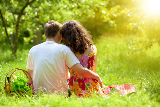 Young Couple Sitting Back To Camera On Picnic Blanket