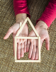 Hands holding model house made of wooden sticks