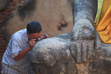 Archaeology man looking pass magnifier lens on old buddha statue in heritage site Ayuthaya Thailand