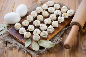 Raw pelmeni, eggs, bay leaves and rolling pin on a wooden table