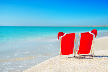 Santa hat on chaise longues at white sand beach against the sea