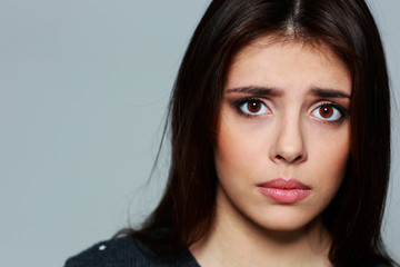 Naklejka premium Closeup portrait of a young sad woman on gray background