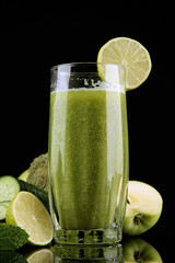 Glass of green vegetable juice and vegetables isolated on black