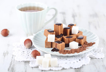 Many toffee on plate and cup of tea on napkin on wooden table