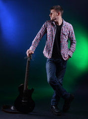 Fototapeta premium Young musician with guitar on dark color background