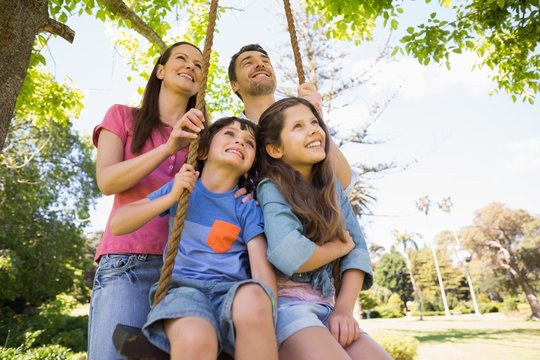 Happy Couple Pushing Kids On Swing