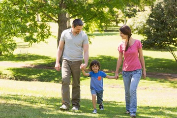 Naklejka na ściany i meble Family of three holding hands and walking at park