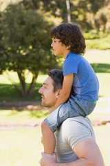 Smiling man carrying son on his shoulders in park