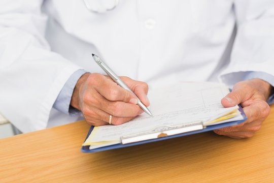 Doctor sitting at his desk writing on clipboard