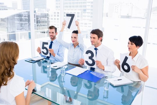 Group of panel judges holding score signs in front of woman